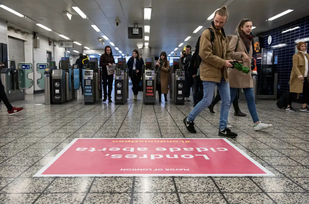 A commuter looks down at a floor vinyl in Stockwell tube station. The vinyl reads 'Londres, cidade aberta'