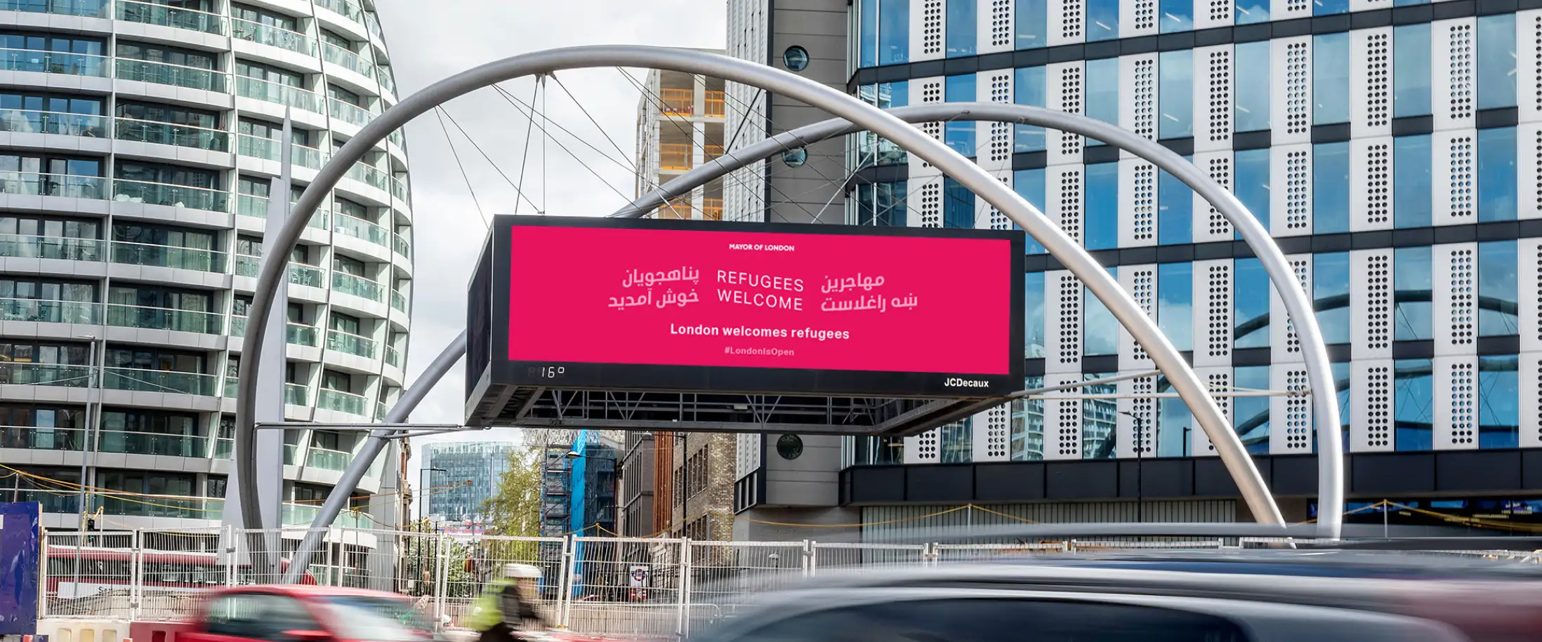 A bright pink LED display advert on a busy London street with text in Dari, English and Pashto reading 'Refugees Welcome'